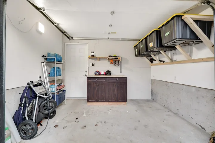 Garage featuring a concrete floor, built-in dark wood-finish cabinetry, white interior door, and overhead storage shelving