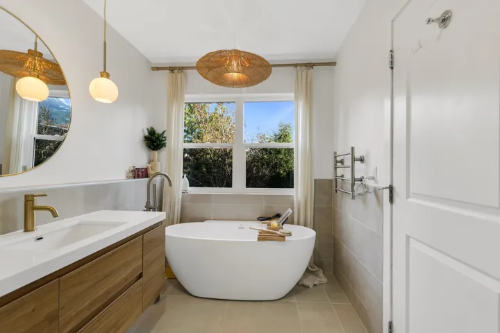 Freestanding soaking tub with a window backdrop, complemented by a wood-finish vanity with an integrated sink