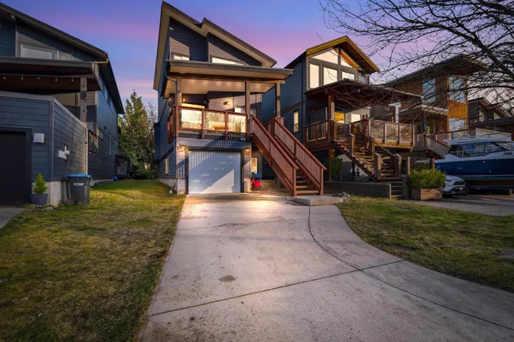 Contemporary multi-level residence featuring dark siding, a prominent attached two-car garage, and multiple exterior balconies with glass railings