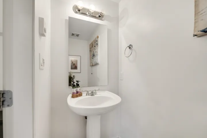 Pedestal sink with chrome faucet, complemented by an overhead vanity light fixture