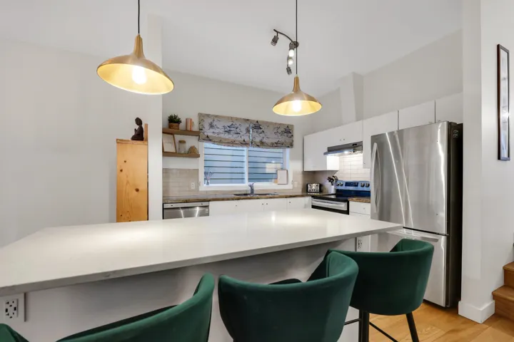 Kitchen featuring a large central island with a light-toned countertop, stainless steel appliances, white cabinetry, and a tile backsplash