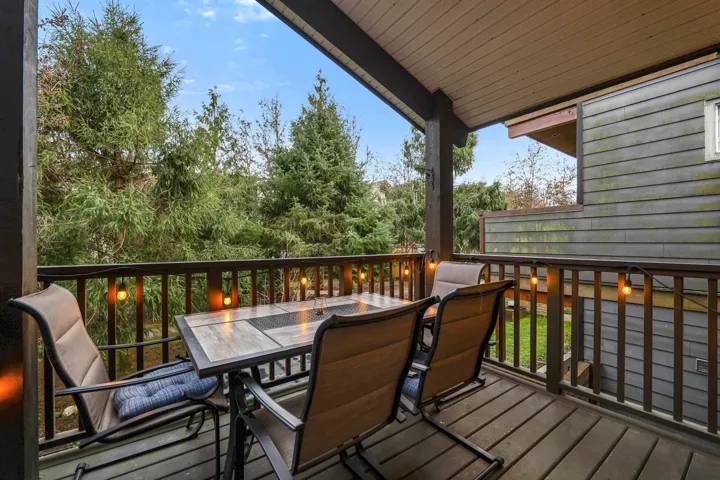 Covered outdoor deck featuring a wood-finish floor, dark wood railing, and a sloped wood-paneled ceiling