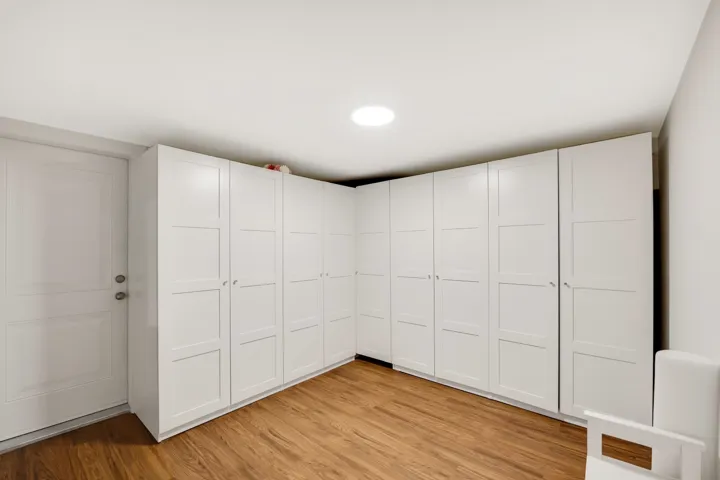 Wraparound white built-in cabinetry with panel detailing, wood-finish flooring, and recessed ceiling lighting