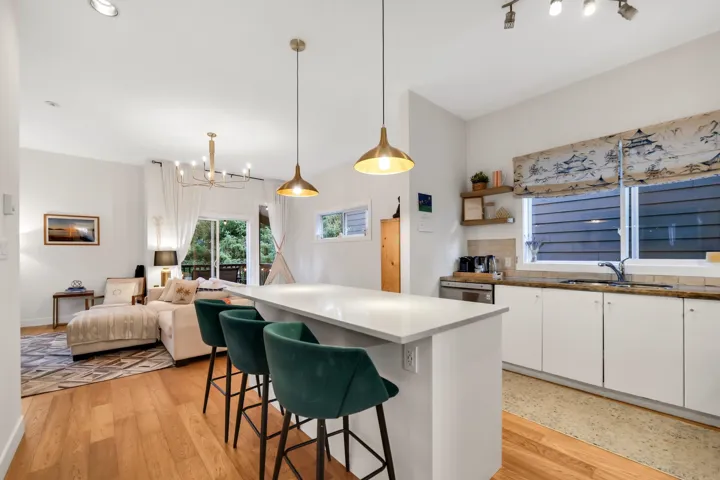 Open-concept living space featuring wood-finish flooring, a kitchen island with pendant lighting, white cabinetry, a built-in stainless steel dishwasher, and a sliding glass door opening to an exterior area
