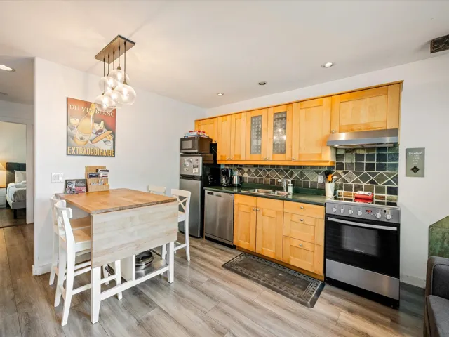 Kitchen with appliances with stainless steel finishes, under cabinet range hood, a sink, light wood-style floors, and tasteful backsplash