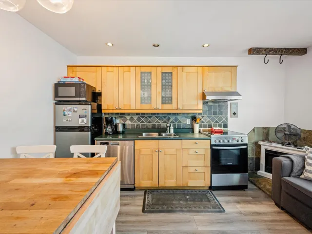 Kitchen with stainless steel appliances, a sink, under cabinet range hood, light brown cabinetry, and decorative backsplash