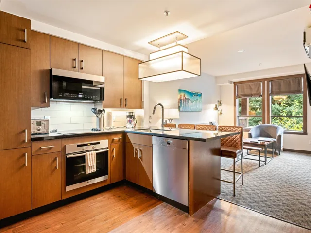 Kitchen with decorative backsplash, stainless steel appliances, a peninsula, brown cabinetry, and light wood-style floors