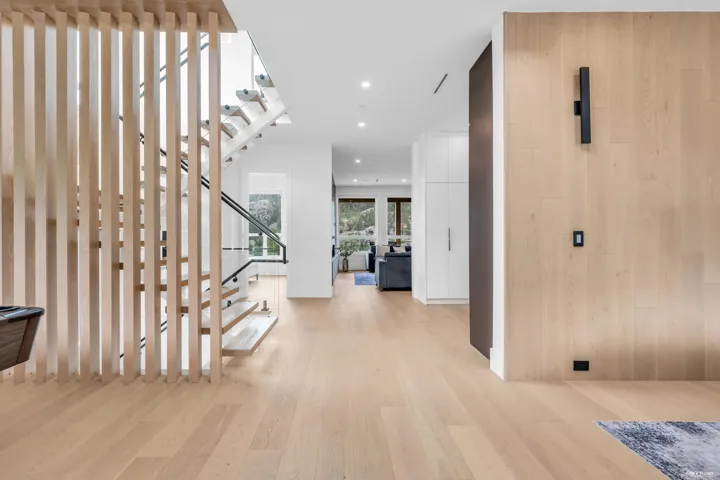 Open-concept interior featuring light wood-finish flooring, a contemporary staircase with glass railing, and a slatted wood room divider