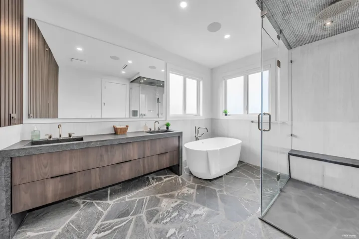 Modern bathroom featuring a freestanding soaking tub, a spacious glass-enclosed shower, a double vanity with dark wood cabinetry, a large wall-mounted mirror, and unique irregular-patterned stone flooring