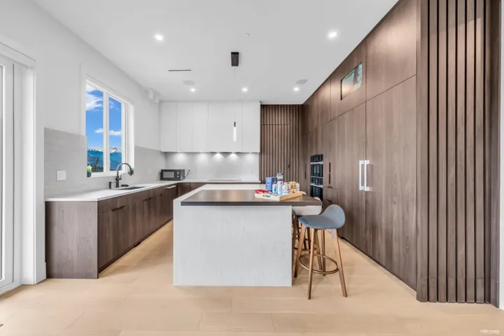 Modern kitchen featuring a large island, contemporary wood-finish cabinetry, light-toned flooring, integrated appliances, and a window framing mountain scenery