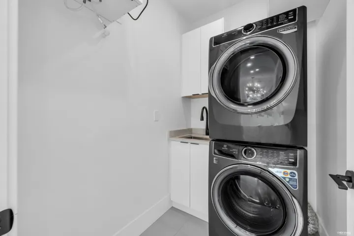 Dedicated laundry area featuring a stacked washer and dryer, under-cabinet sink, matte black faucet, white cabinetry, and a light-toned countertop