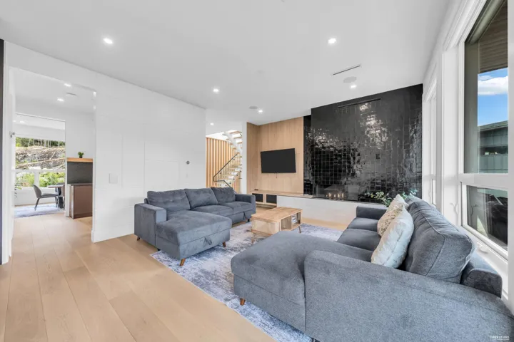 Open concept living area featuring wood-finish flooring, a contemporary fireplace with black tile surround, a built-in media console, large windows, and recessed lighting