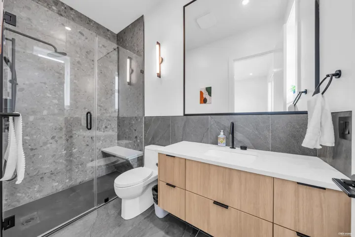 Contemporary bathroom featuring a spacious glass-enclosed shower with full-height stone-look tile, a built-in shower bench, and a matte black rainfall showerhead