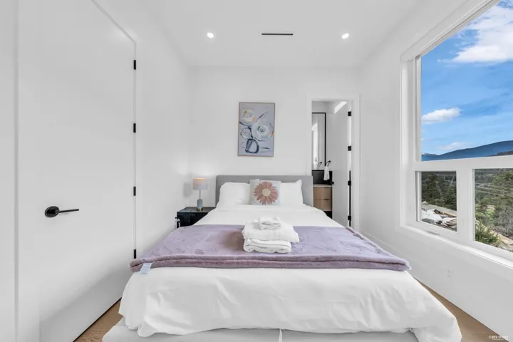 Bright sleeping area featuring wood-finish flooring, a contemporary window providing expansive outdoor scenery, a recessed ceiling light, and a white interior door with matte black hardware