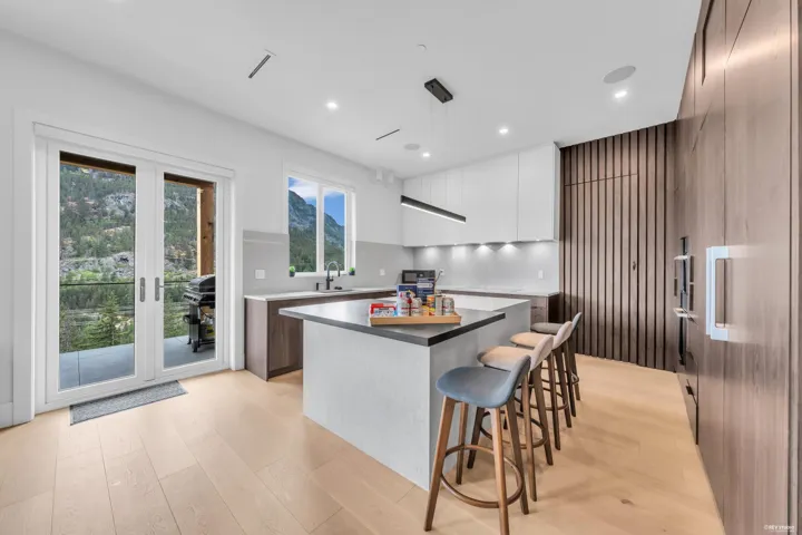 Modern kitchen featuring a central island with seating, light wood-finish flooring, white upper cabinetry, and a dark wood-paneled feature wall