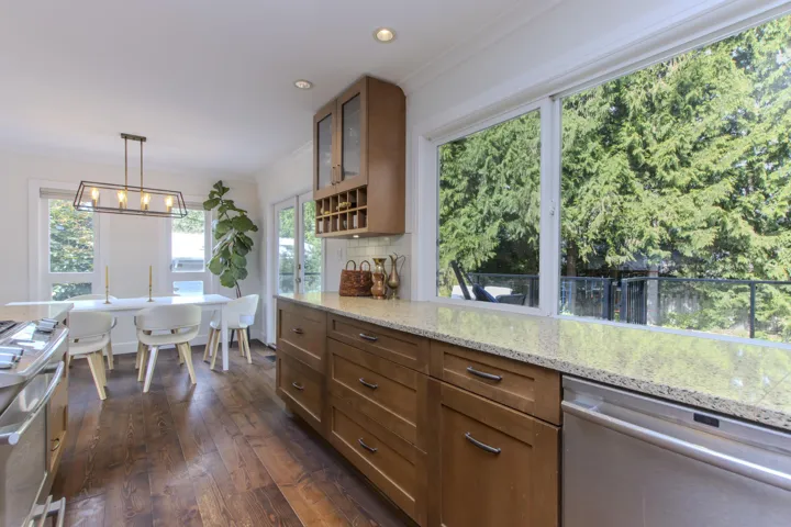 Kitchen with brown cabinets, pendant lighting, stainless steel appliances, ornamental molding, and glass insert cabinets