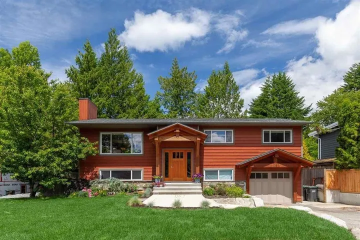 Bi-level home with a front yard, an attached garage, a chimney, and driveway