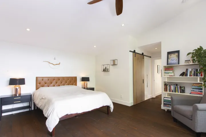 Bedroom with a barn door, lofted ceiling, dark wood-type flooring, a ceiling fan, and recessed lighting