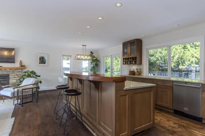 Kitchen featuring a breakfast bar, light stone counters, stainless steel dishwasher, dark wood finished floors, and crown molding