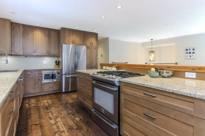 Kitchen with stainless steel appliances, light stone counters, dark wood finished floors, pendant lighting, and brown cabinets