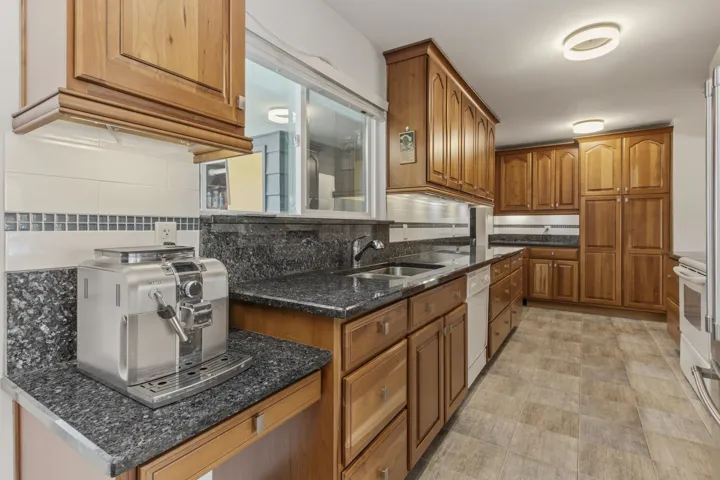 Functional kitchen featuring wood cabinetry, granite-finish countertops, tile flooring, and integrated stainless steel sink