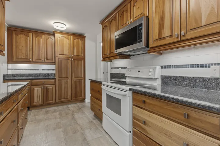 Kitchen featuring extensive wood cabinetry, dark speckled countertops, and a full suite of appliances including a range and microwave