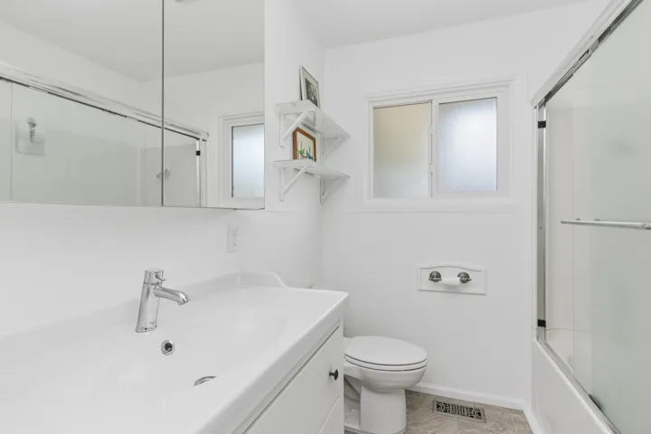 Bathroom featuring a white vanity with integrated sink, chrome faucet, window with frosted glass, and a tub-shower combination with sliding glass doors