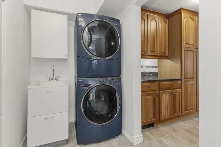 Laundry area featuring a stackable washer and dryer, utility sink, white wall cabinet, and wood-finish flooring