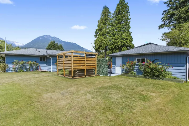 Expansive backyard featuring two blue-sided structures with dark roofs and a prominent wooden hot tub enclosure