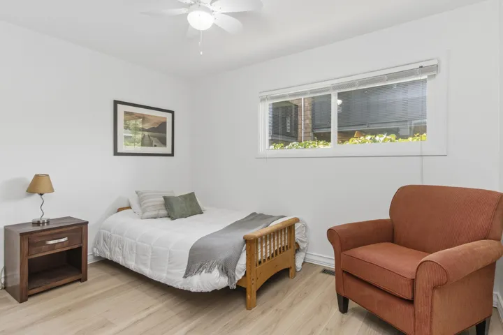 White interior walls with light wood-finish flooring, a ceiling fan, and a window featuring blinds