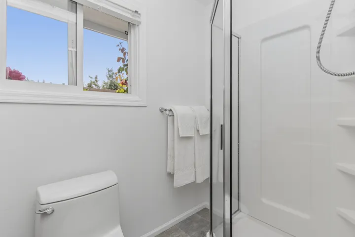 Bathroom featuring a glass-enclosed shower, white ceramic toilet, and a window with white trim
