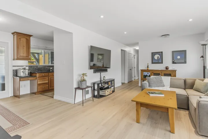 Light wood-finish flooring throughout, recessed lighting, and a kitchen area featuring wood cabinetry, dark countertops, and a subway tile backsplash