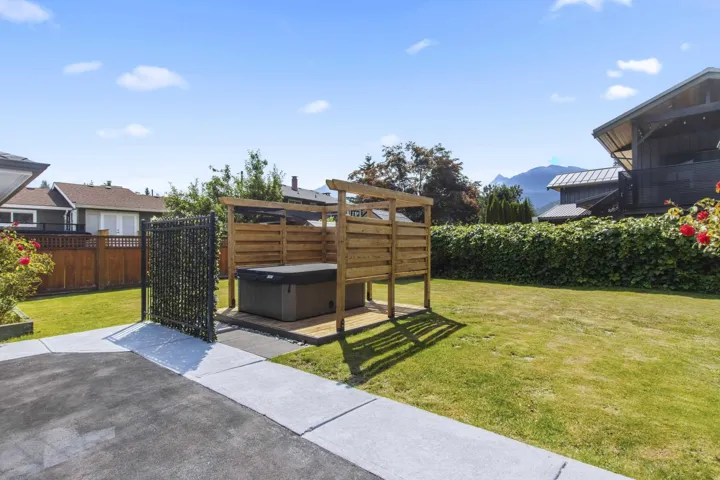 Backyard featuring a built-in hot tub with a slatted privacy enclosure, manicured lawn, paved patio, and a mountain backdrop