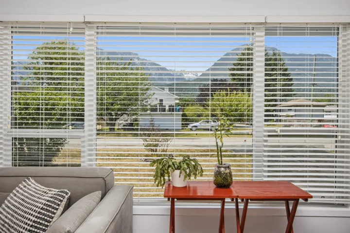 Large windows with white horizontal blinds frame a mountain backdrop and neighborhood scenery