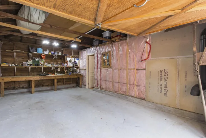 Spacious garage featuring a concrete floor, exposed wood beam ceiling, built-in workbench, and overhead lighting