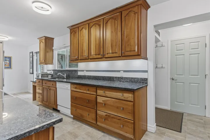 Kitchen featuring wood cabinetry, dark speckled countertops, and a white tile backsplash with decorative accent
