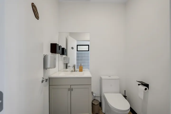 White-painted interior featuring a single vanity with a light gray cabinet, a chrome faucet, and a wall-mounted mirror