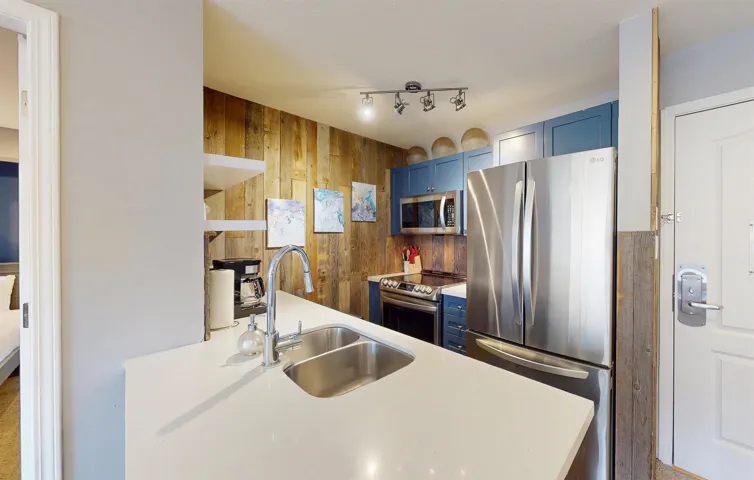 Kitchen with appliances with stainless steel finishes, blue cabinets, light countertops, wood walls, and a sink