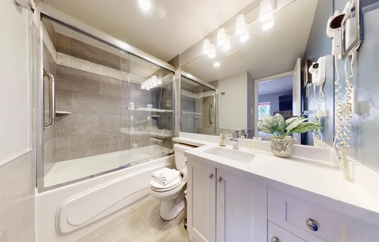 Bathroom with toilet, visible vents, bath / shower combo with glass door, and vanity