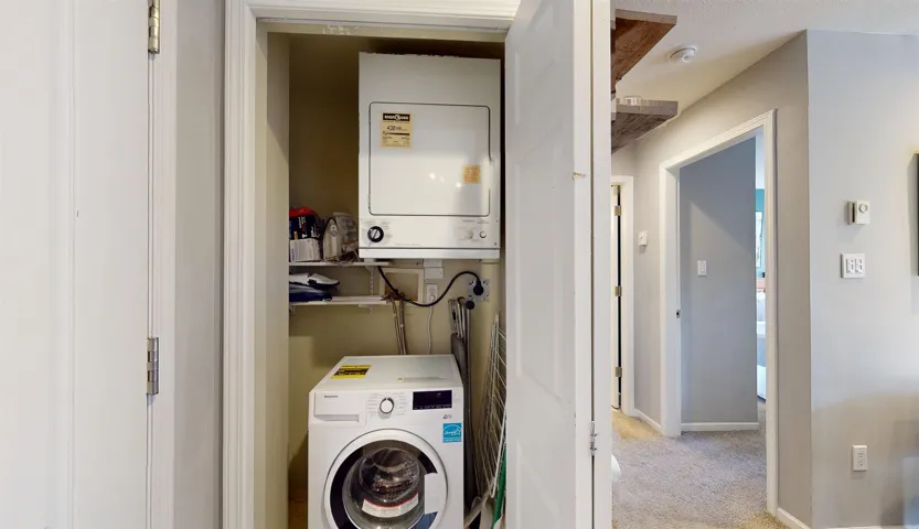 Laundry area featuring light colored carpet, stacked washer and dryer, laundry area, baseboards, and water heater