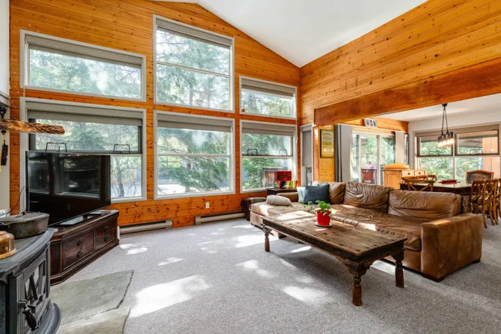 Vaulted ceiling living space featuring extensive wood paneling, a wall of large windows, and a built-in wood-burning stove