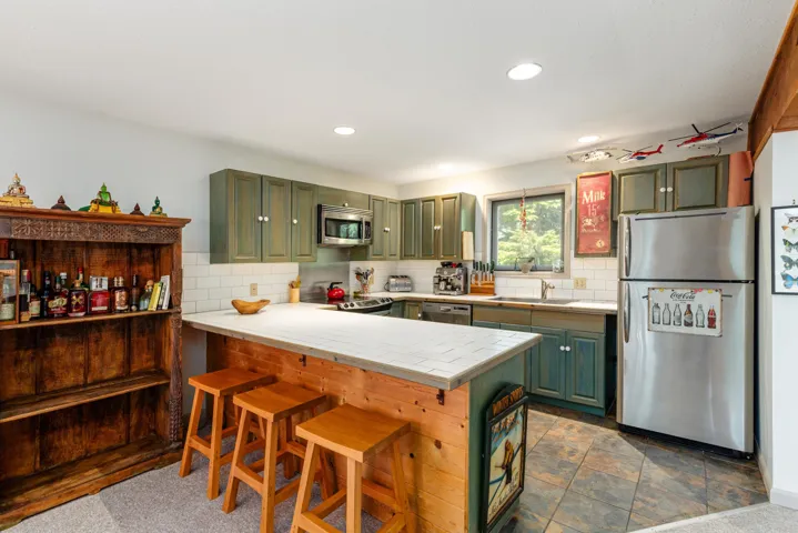 Kitchen with wood-finish island seating, tile flooring, green cabinetry, white subway tile backsplash, and stainless steel appliances