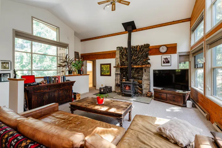 Living area featuring a stone fireplace with a wood-burning stove, vaulted ceilings with wood beams, and a ceiling fan