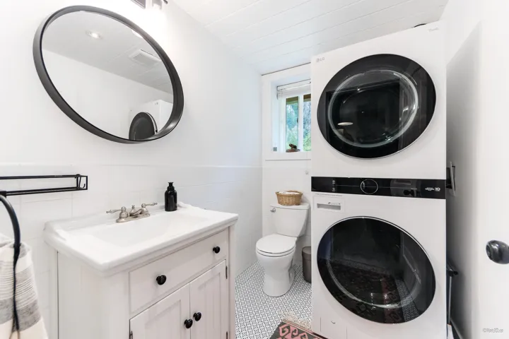 Bathroom featuring vanity, tile patterned floors, stacked washer and clothes dryer, wainscoting, and tile walls