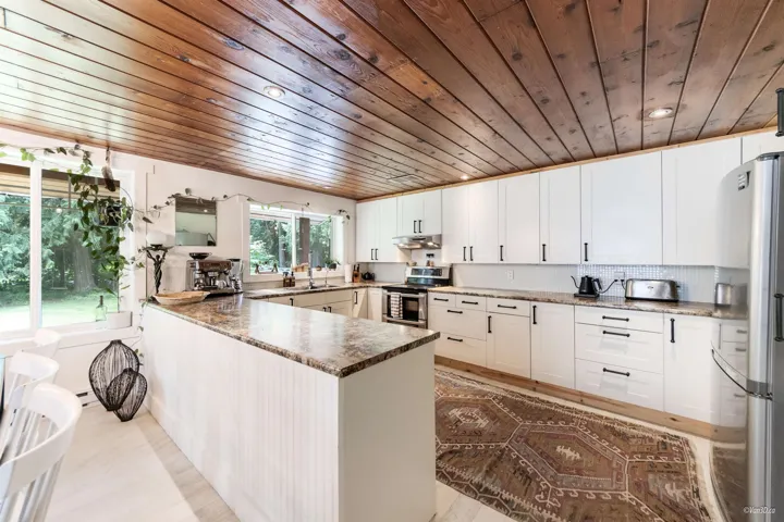 Kitchen with a peninsula, stainless steel appliances, white cabinetry, wood ceiling, and decorative backsplash