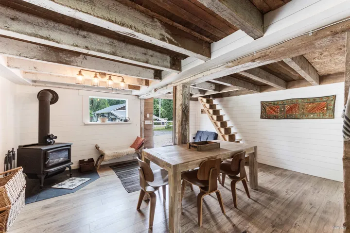 Dining space with wood walls, a wood stove, wood finished floors, and beamed ceiling