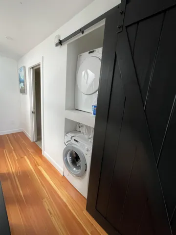 Washroom featuring a barn door, light wood-type flooring, and stacked washer and clothes dryer