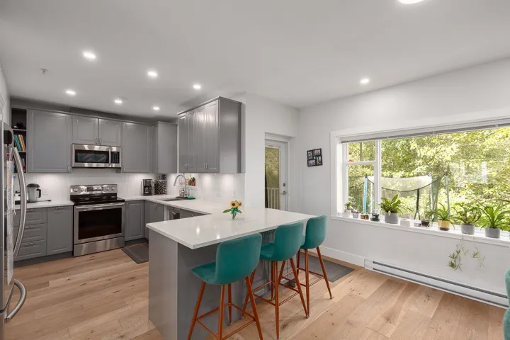 Kitchen with gray cabinetry, stainless steel appliances, a baseboard heating unit, light wood finished floors, and recessed lighting