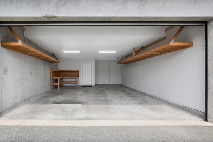 Concrete garage flooring featuring overhead shelving, built-in workbench, and white painted walls