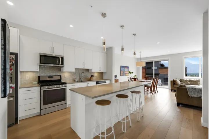 Modern kitchen featuring a central island with countertop seating, stainless steel appliances, white cabinetry, and wood-finish flooring
